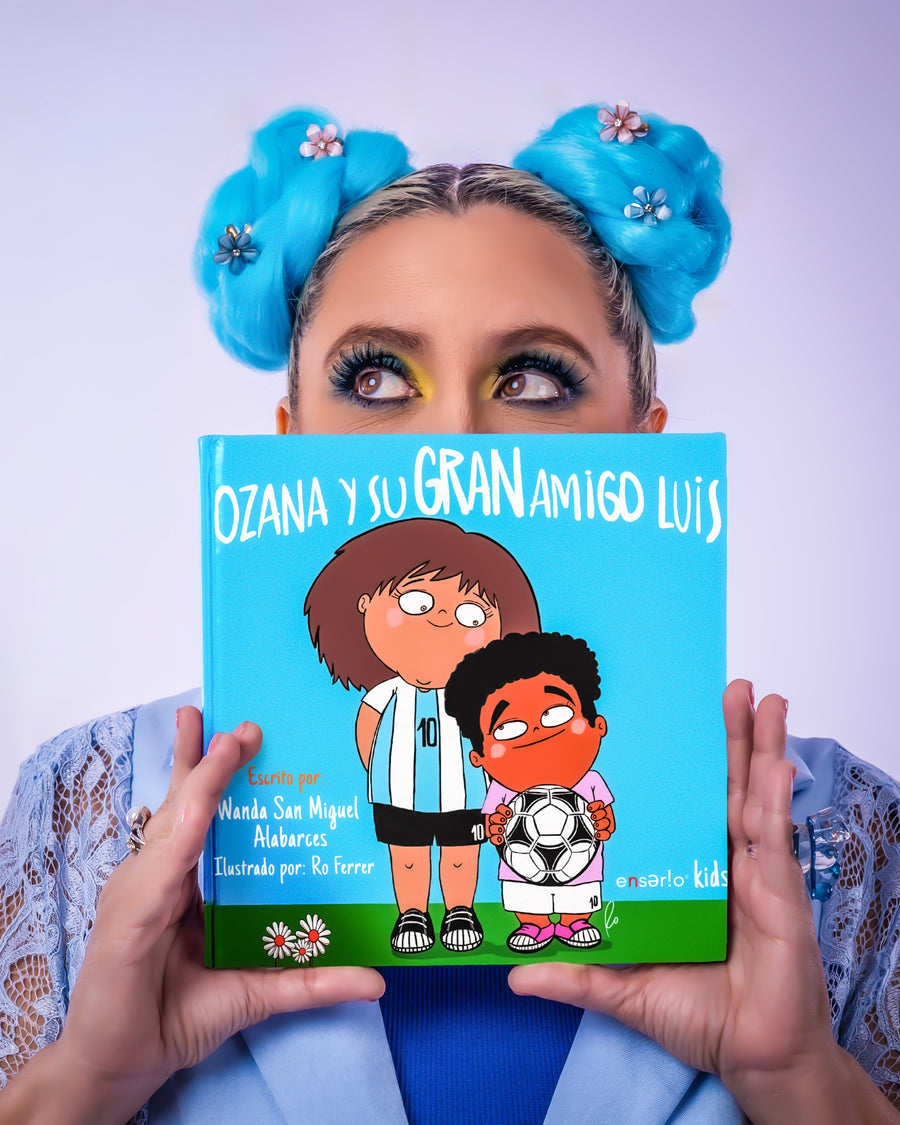 Joven con moños azules sostiene el libro Ozana y su Gran Amigo Luis de Mundo Ozana frente a su cara.